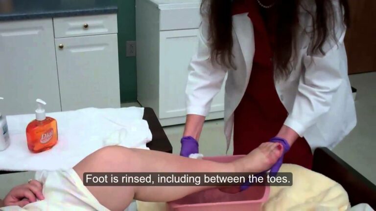 A person in a white coat rinses another person's foot in a pink basin. The caption on the image reads: "Foot is rinsed, including between the toes.
