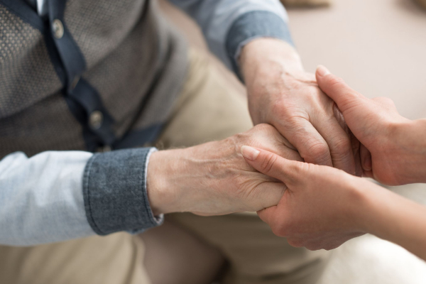 A person holds and gently supports the hands of an elderly individual, conveying care and support.