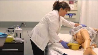 A healthcare professional demonstrates a procedure on a medical mannequin in a clinical setting.
